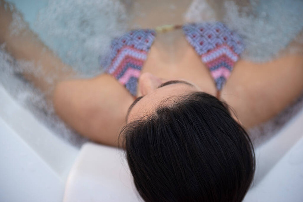 Vista superior da bela mulher de biquíni em um banho de hidromassagem,, em um maiô. Conceito: procedimentos de spa, massagens corporais, creme de spa, relaxamento, tratamentos de água de spa, piscina. - Foto, Imagem