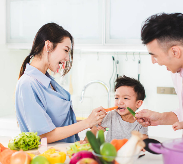 parent feeding boy a piece of  carrot in kitchen - Photo, Image