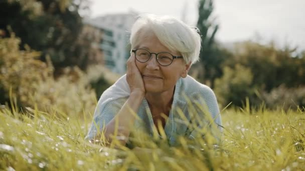 ηλικιωμένη γκρίζα μαλλιά γυναίκα απολαμβάνοντας την ηλιόλουστη ημέρα του φθινοπώρου στο πάρκο - Πλάνα, βίντεο