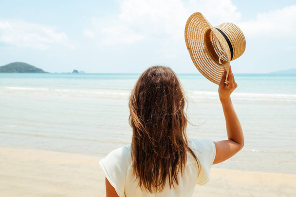 Beautiful young woman raises her hat on a sunny beach - Fotó, kép