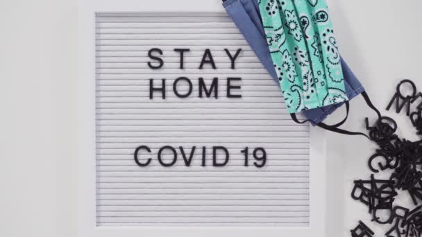 STAY HOME ja COVID-19 allekirjoittaa ilmoitustaululla kotitekoinen kasvonaamio. - Materiaali, video