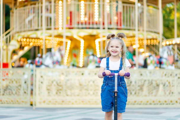niña feliz montando un scooter en verano en un parque de atracciones, infancia feliz - Foto, Imagen