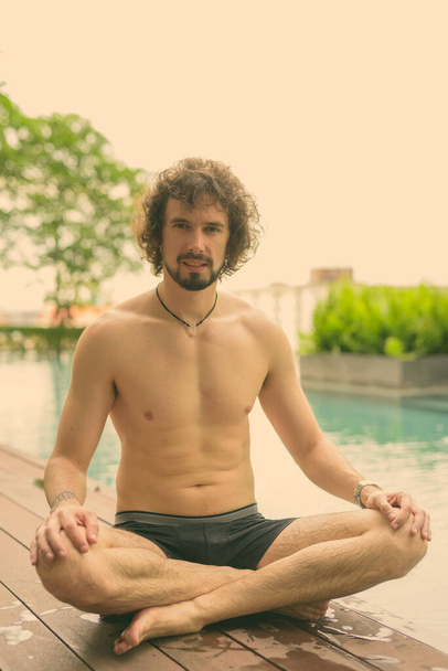 Portrait of handsome bearded man with curly hair shirtless relaxing beside the swimming pool in the city of Bangkok, Thailand - Photo, Image