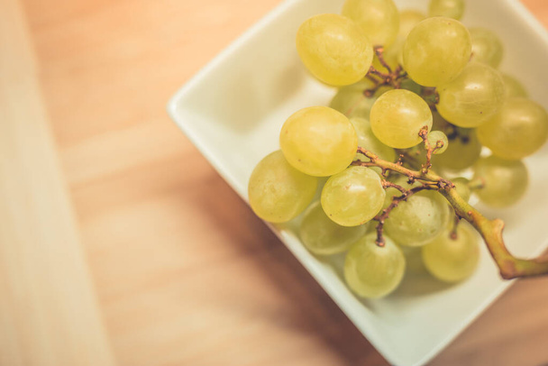 White bowl with green grapes on wooden table, soft light - Foto, Imagem