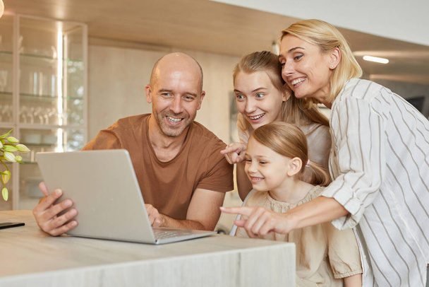 Teplý-tónovaný portrét šťastné moderní rodiny pomocí notebooku spolu při mluvení video chat s příbuznými v útulném interiéru domu, kopírovat prostor - Fotografie, Obrázek