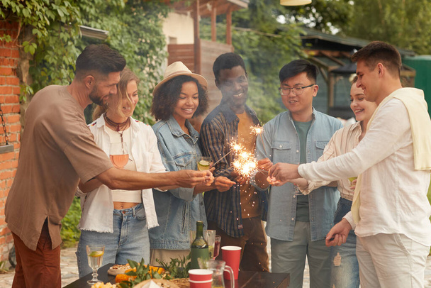 Gruppo multietnico di giovani che accendono scintille mentre si godono la festa estiva sulla terrazza all'aperto, copia lo spazio - Foto, immagini
