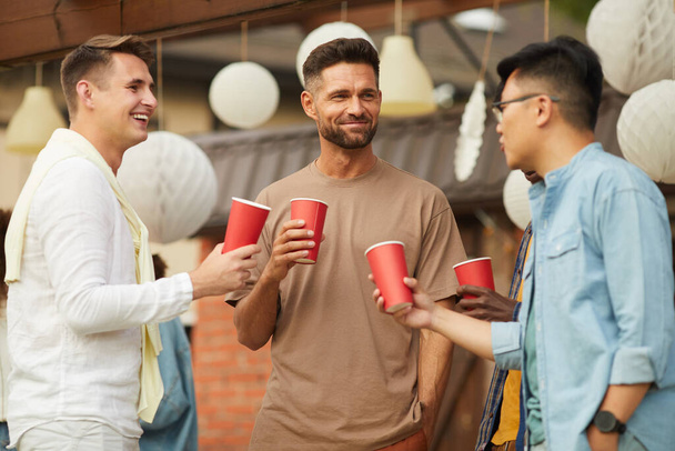 Retrato de la cintura hacia arriba de hombres jóvenes que beben cerveza y eclosionan durante la fiesta al aire libre en verano, espacio para copiar - Foto, imagen