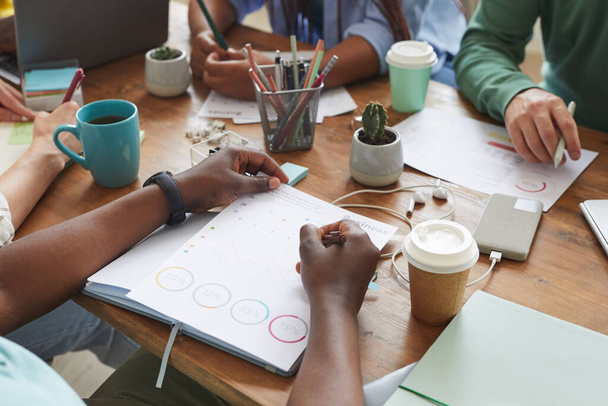 Close up of multi-ethnic group of people working together at cluttered table with cups, mugs and stationary items, teamworking or studying concept, copy space - Photo, Image