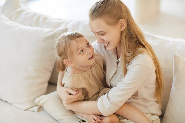 Caliente retrato de ángulo alto tonificado de una adolescente sonriente sosteniendo a una linda hermana pequeña mientras está sentada en un acogedor sofá blanco en casa, espacio para copiar - Foto, Imagen
