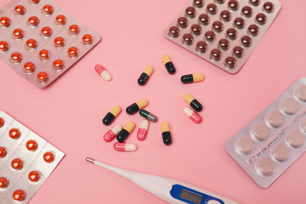 Top down view at flat lay of medicine capsules, pills and thermometer on pink background, covid and flu concept, copy space - Foto, Imagem