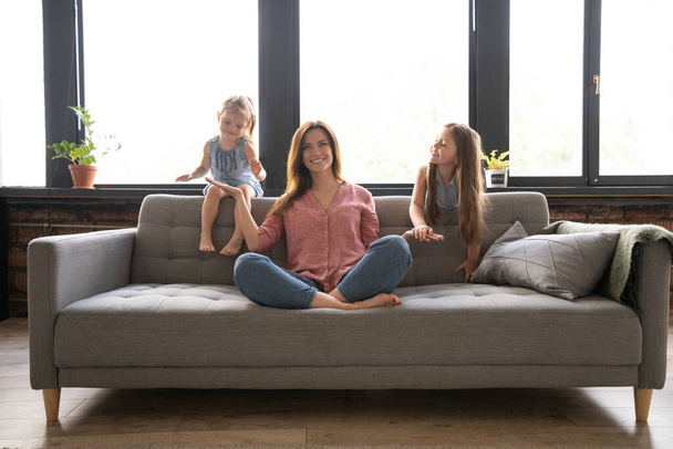 Calm woman concentrating on yoga exercises on couch at home while two noisy kids laughing, running - Fotoğraf, Görsel