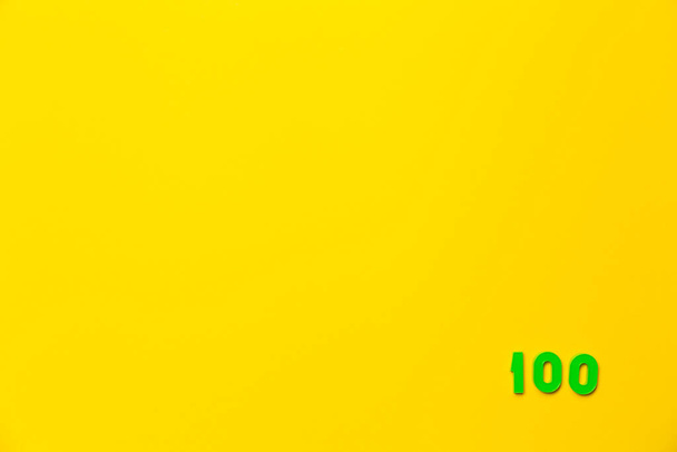 A zöld és rózsaszín műanyag játék száma száz található a jobb alsó sarokban egy sárga háttér. - Fotó, kép