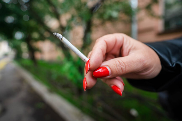 A mão de uma mulher com uma manicure brilhante segura um cigarro ardente, fazendo campanha para parar de fumar - Foto, Imagem