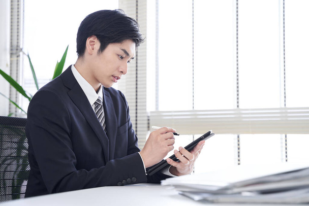 Японський бізнесмен - чоловік використовує табличку у своєму офісі, щоб перетворити паперові документи на дані. - Фото, зображення