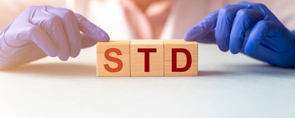 木製のブロックは保護医師の手袋で単語STDを形成します。医学的概念。先生 - 写真・画像