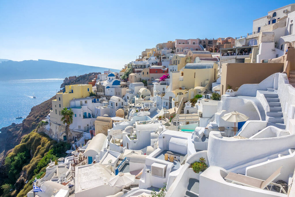 Greece. Sunny summer day in Santorini. Oia buildings and terraces with flowers on the caldera with seaview - 写真・画像