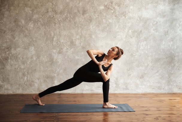 Yogi femme d'âge moyen pratiquant le yoga, debout dans la pose Parsvakonasana, exercice d'angle latéral, séance d'entraînement à la maison ou en studio de yoga, pleine longueur. Concept de pleine conscience et mode de vie sain - Photo, image