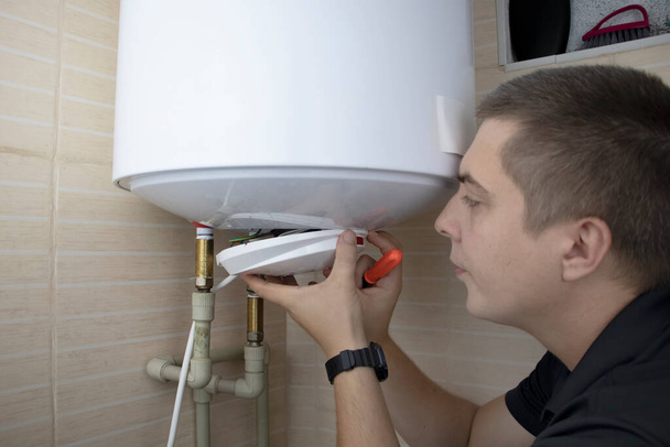 The boiler repair technician uses an adjustable wrench to unscrew or tighten the nut on the pipe. Installing a water heater or dismantling a damaged boiler for later repair. - Photo, Image