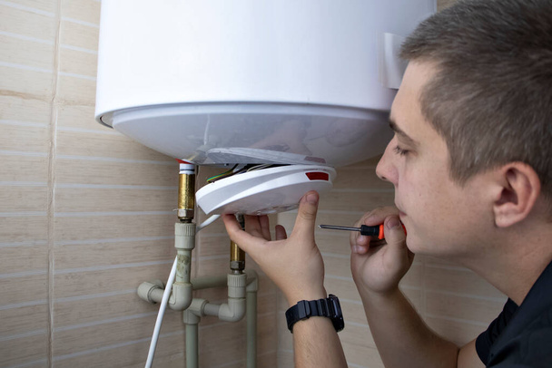 The boiler repairman checks the electronics in the water heater. Professional assistance and technical support concept - Photo, Image