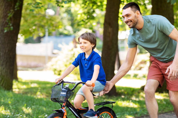 father teaching little son to ride bicycle at park - Φωτογραφία, εικόνα