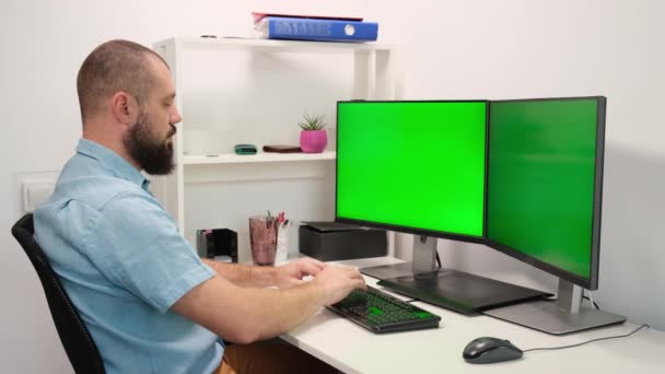 Man type op het toetsenbord op twee monitoren met het groene scherm. - Video