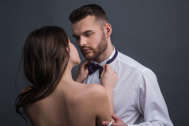 Passionate couple, romantic lovers. Woman holds mans bowtie, bow tie. Sexy elegant people in tender passion. - Photo, Image