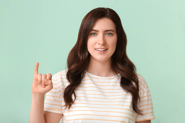 Joven mujer muda sorda usando lenguaje de señas sobre fondo de color - Foto, Imagen
