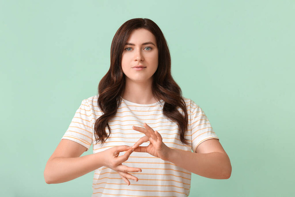 Jovem mulher surda muda usando linguagem de sinais em fundo de cor - Foto, Imagem