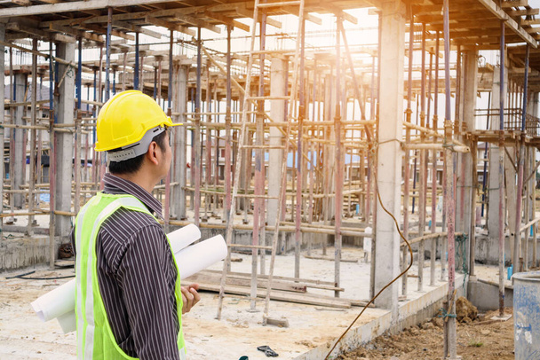 Asiático hombre de negocios ingeniero de construcción trabajador en casco de protección y planos de papel en la mano en la obra de la casa - Foto, Imagen