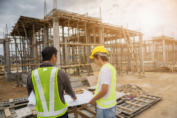 Asiatischer Geschäftsmann Bauleiter und Ingenieur mit Schutzhelm halten auf Hausbaustelle Baupläne in der Hand - Foto, Bild
