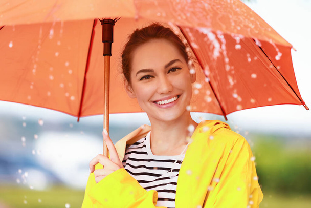 Όμορφη νεαρή γυναίκα με ομπρέλα φορώντας αδιάβροχο σε εξωτερικούς χώρους - Φωτογραφία, εικόνα