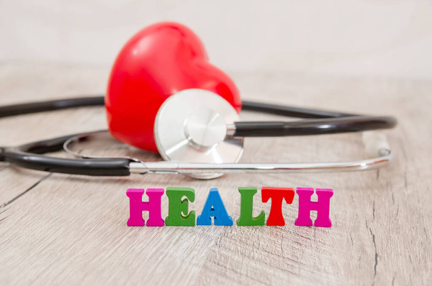 the word "health" made of colored letters, a red heart and a stethoscope. Wooden background. - Photo, Image