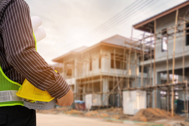 Asiático hombre de negocios ingeniero de construcción trabajador en casco de protección y planos de papel en la mano en la obra de la casa - Foto, imagen