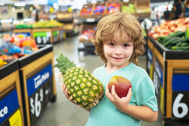 Kid hold pineapple in supermarket. Sale, consumerism and kids concept. - Фото, изображение