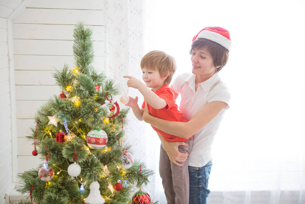 Mutter mit Sohn schmückt gemeinsam Weihnachtsbaum, Bauernhausgestaltung - Foto, Bild