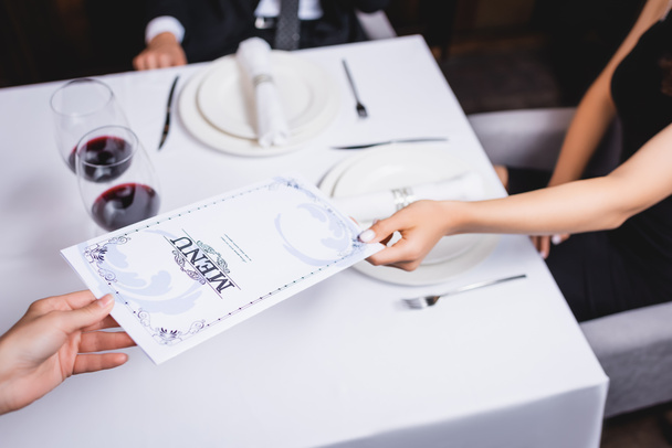 Обрезанный вид официантки, дающей меню молодой женщине в ресторане  - Фото, изображение