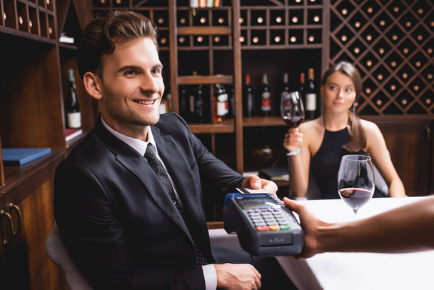 Szelektív fókusz a férfi fizet hitelkártyával közelében pincérnő fizetési terminállal és barátnő étteremben  - Fotó, kép
