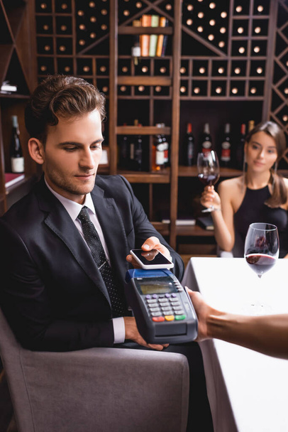 Enfoque selectivo de camarera sosteniendo terminal de pago cerca de hombre con smartphone en restaurante  - Foto, Imagen