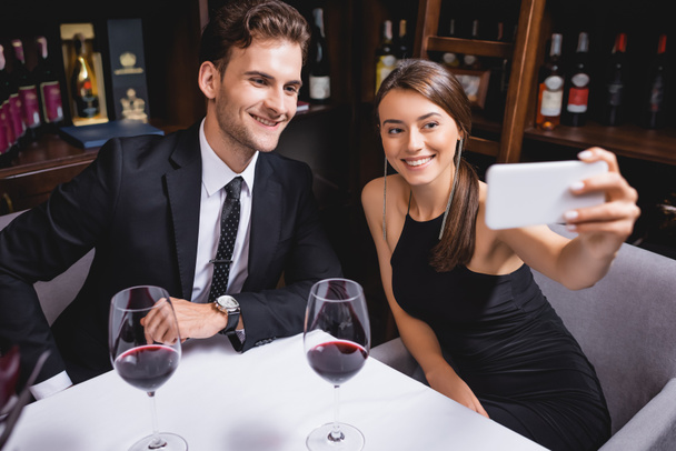 Focus selettivo della giovane coppia che prende selfie vicino a bicchieri di vino nel ristorante  - Foto, immagini
