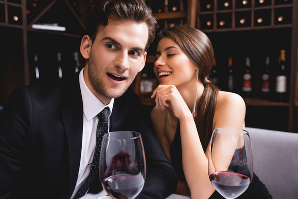 Selective focus of man in suit sitting near glasses of wine and elegant girlfriend in restaurant  - Foto, Imagen