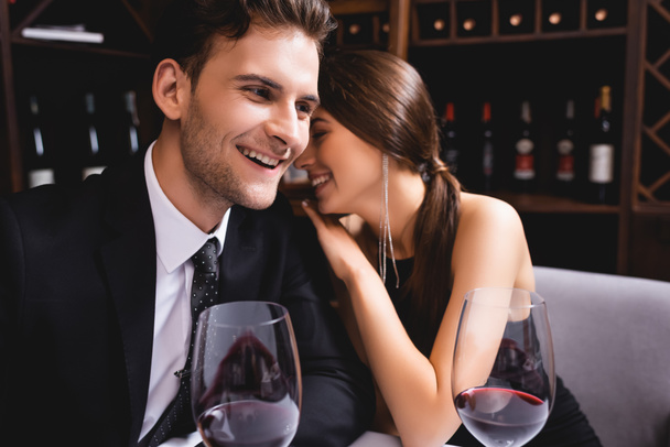Enfoque selectivo de mujer elegante abrazando novio en traje cerca de copas de vino en restaurante  - Foto, Imagen