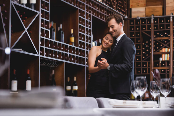 レストランでワインのボトルとラックの近くで踊る若いカップルの選択的な焦点  - 写真・画像