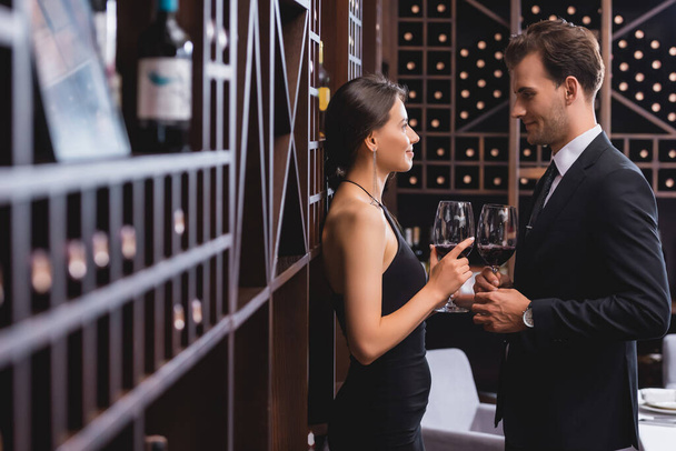 Επιλεκτική εστίαση του κομψού ζευγαριού κοιτάζοντας ο ένας τον άλλο, ενώ κρατώντας ποτήρια του κρασιού στο εστιατόριο  - Φωτογραφία, εικόνα
