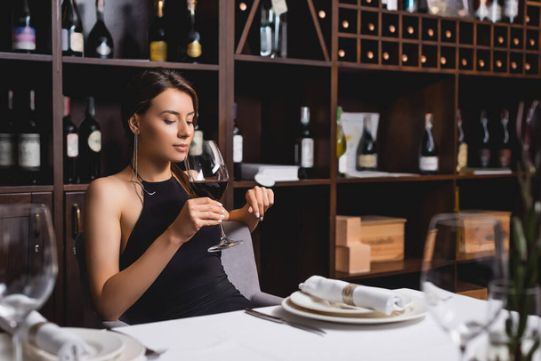 Selective focus of elegant woman holding glass of wine in restaurant  - Фото, изображение