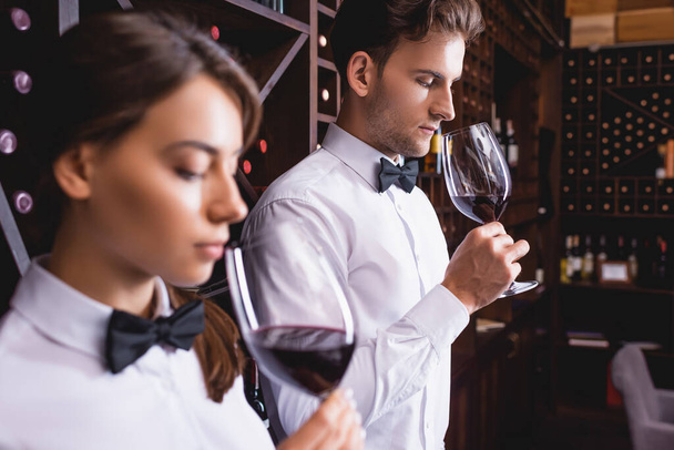 Selective focus of sommelier smelling wine in glass near colleague in restaurant  - 写真・画像