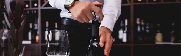 Панорамный снимок сомелье, открывающей бутылку вина возле бокала вина  - Фото, изображение
