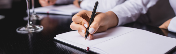 Colpo panoramico di sommelier che scrive su notebook vicino a occhiali in ristorante  - Foto, immagini