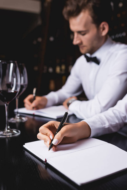 Selective focus of sommeliers writing on notebooks near glasses of wine on table  - Фото, зображення
