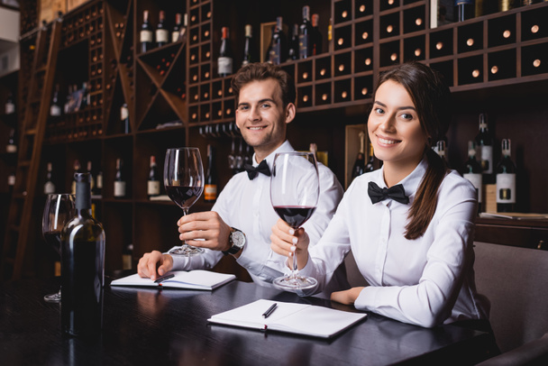 Selective focus of sommeliers with glasses of wine looking at camera in restaurant  - Photo, Image