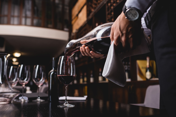 A sommelier holding törölköző szelektív fókusza és a bor üvegbe öntése az asztalon az étteremben  - Fotó, kép